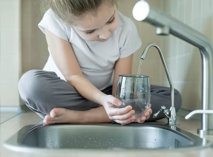 little girl sitting on counter filling water glass from sink filter
