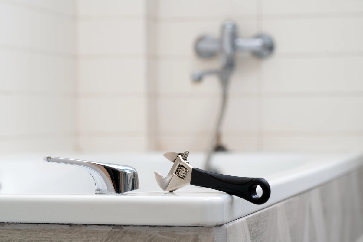 hand tool resting on a bathtub ledge next to bathtub parts