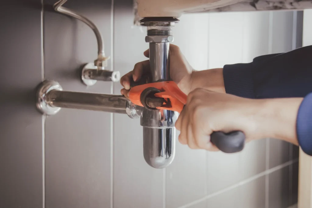 plumber using hand tools to work on sink drain