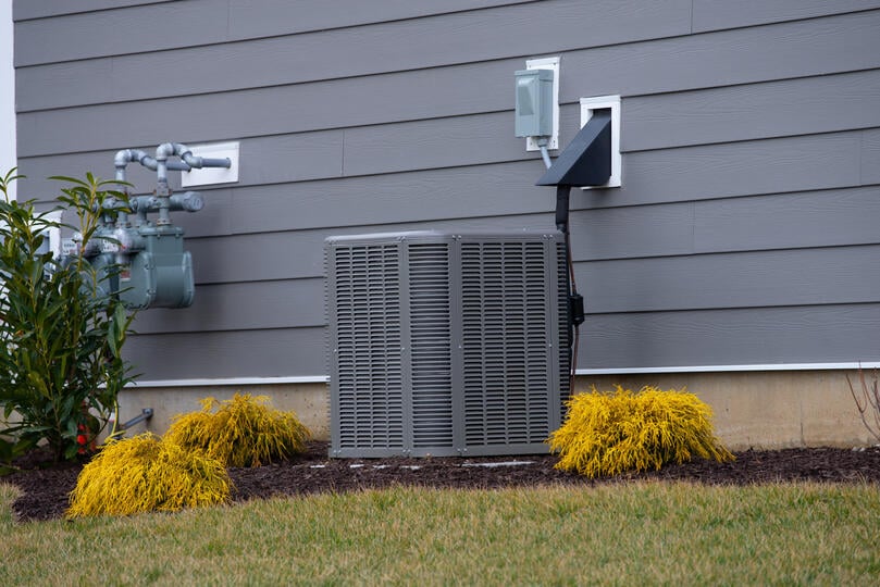 ac condenser-distant view of an ac unit next to a gray sided house