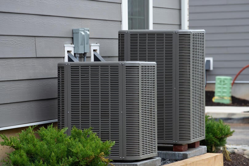 ac condenser-two ac units next to each other next to a gray sided house