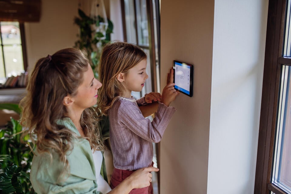 how to calibrate a thermostat-mother and daughter adjusting a thermostat tablet on a wall