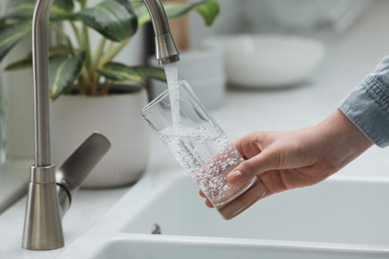 best under sink water filter-woman filling up a drinking glass with water from the kitchen faucet