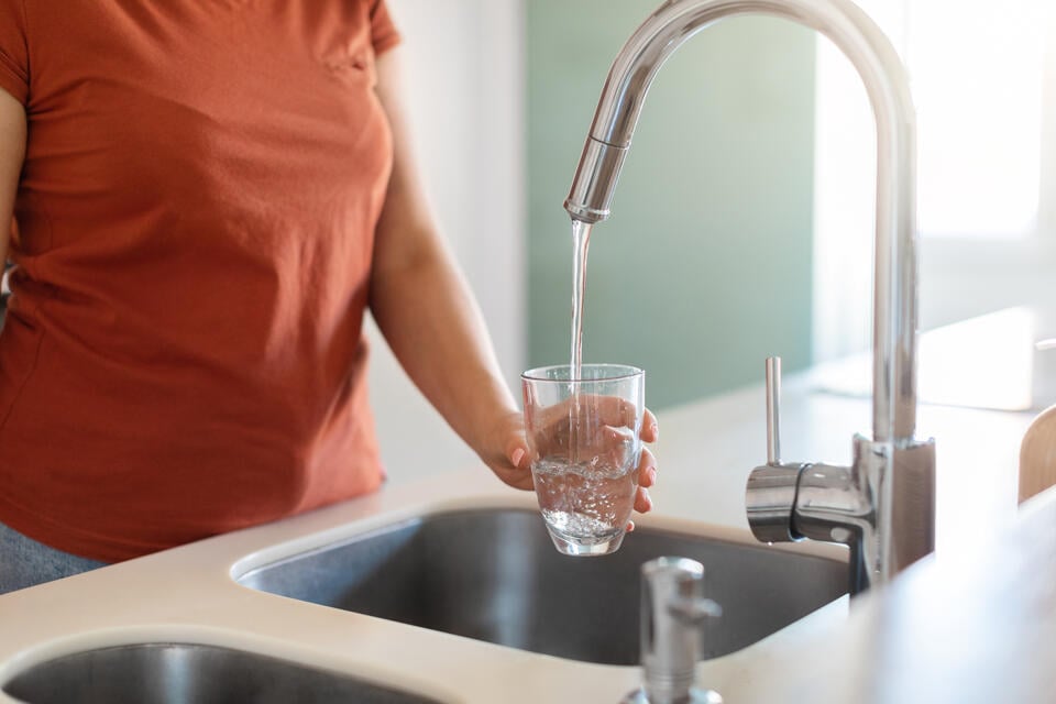 best under sink water filter-woman filling up a glass of water from the kitchen faucet