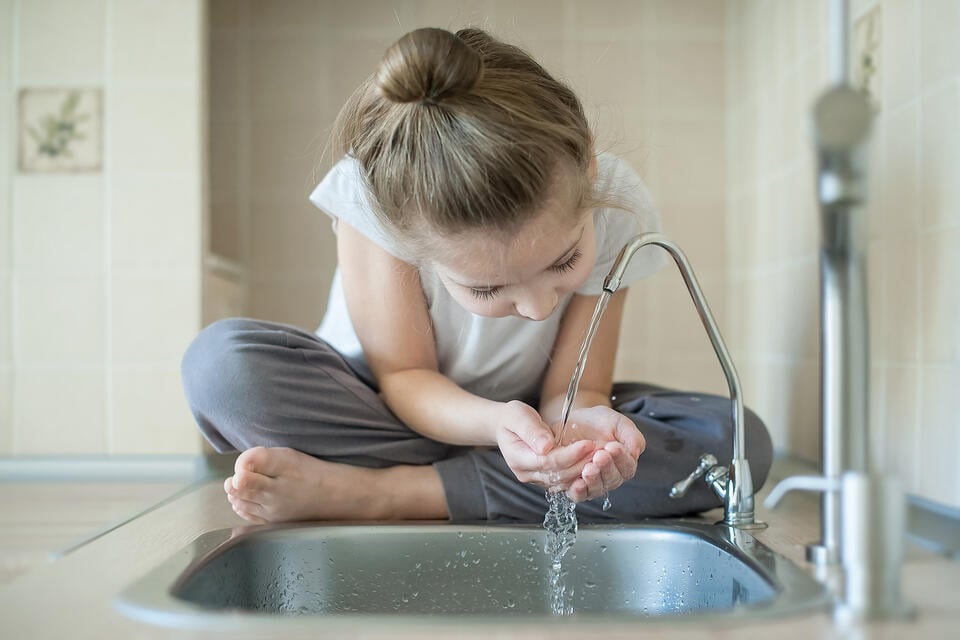 best under sink water filter-young girl drinking water from a water spigot in the kitchen sink