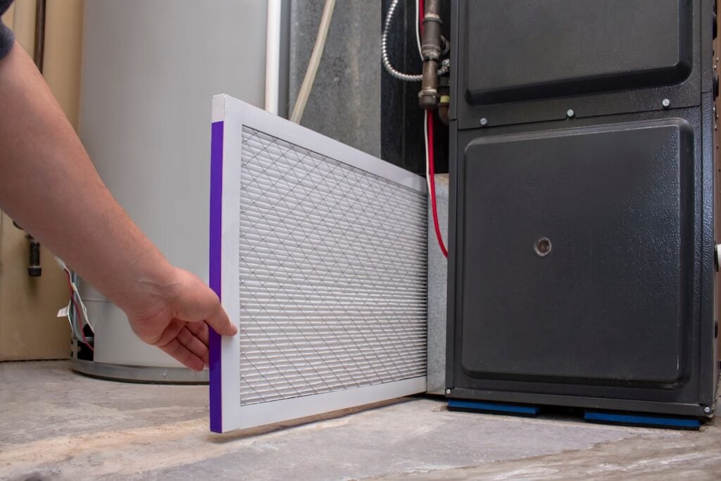 HVAC service technician changing dirty indoor air filter in residential heating and air conditioning system. Home air duct ventilation system maintenance for clean air.