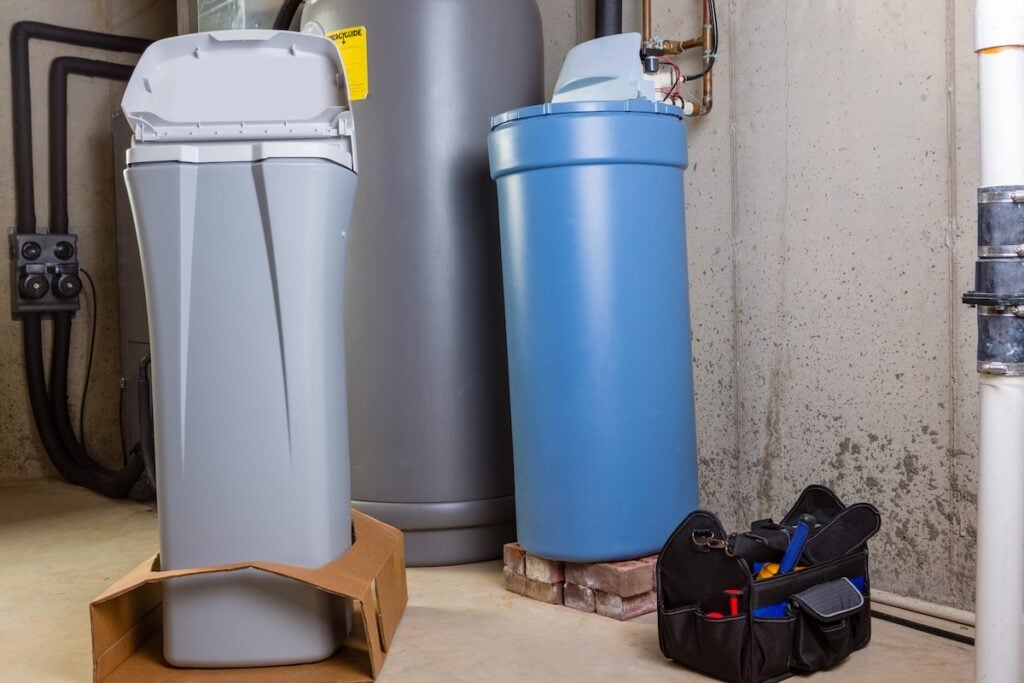 New water softening unit or tank ready alongside the old one for installation to replace it in a utility room with a portable tool kit in a box on the floor salt free water softener