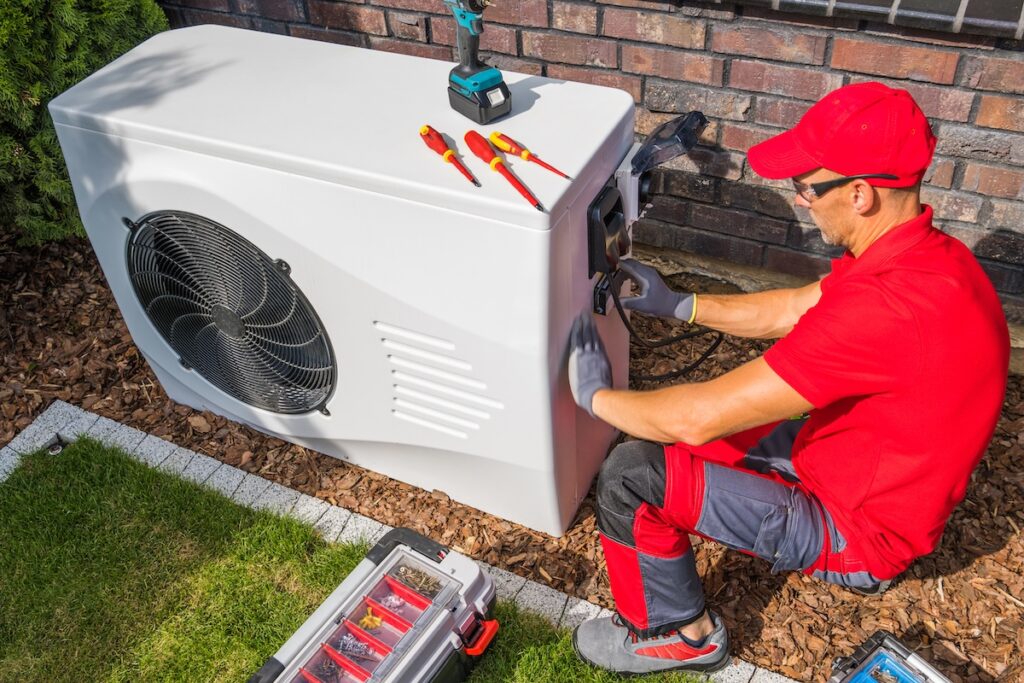 Professional Middle Aged HVAC Technician in Red Uniform Repairing Modern Heat Pump Unit. House Heating and Cooling System Theme.