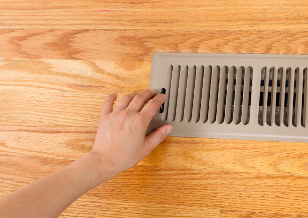 hvac zoning system Horizontal photo of female hand opening up heater floor vent with Red Oak Floors in background